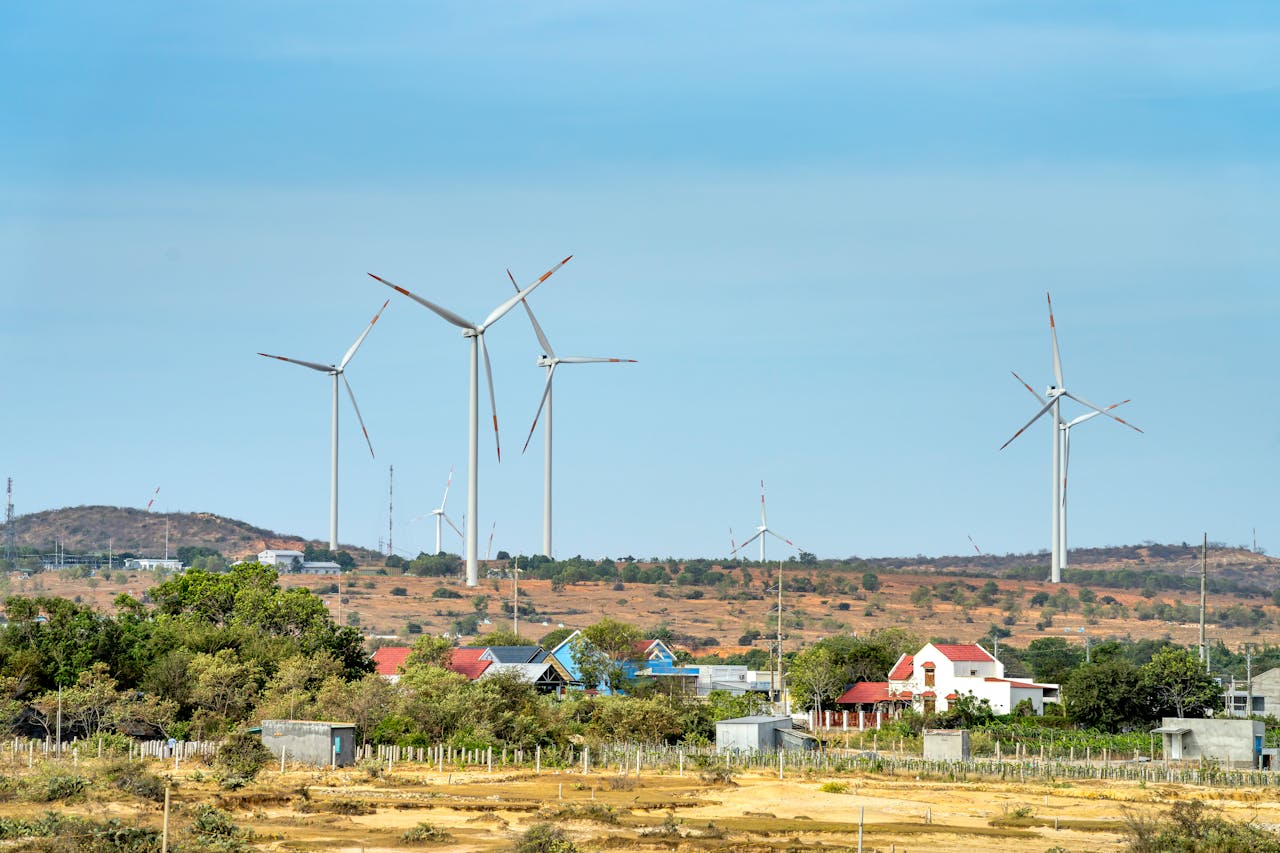 Scenic view of wind generators on land between buildings and mount under cloudy blue sky
